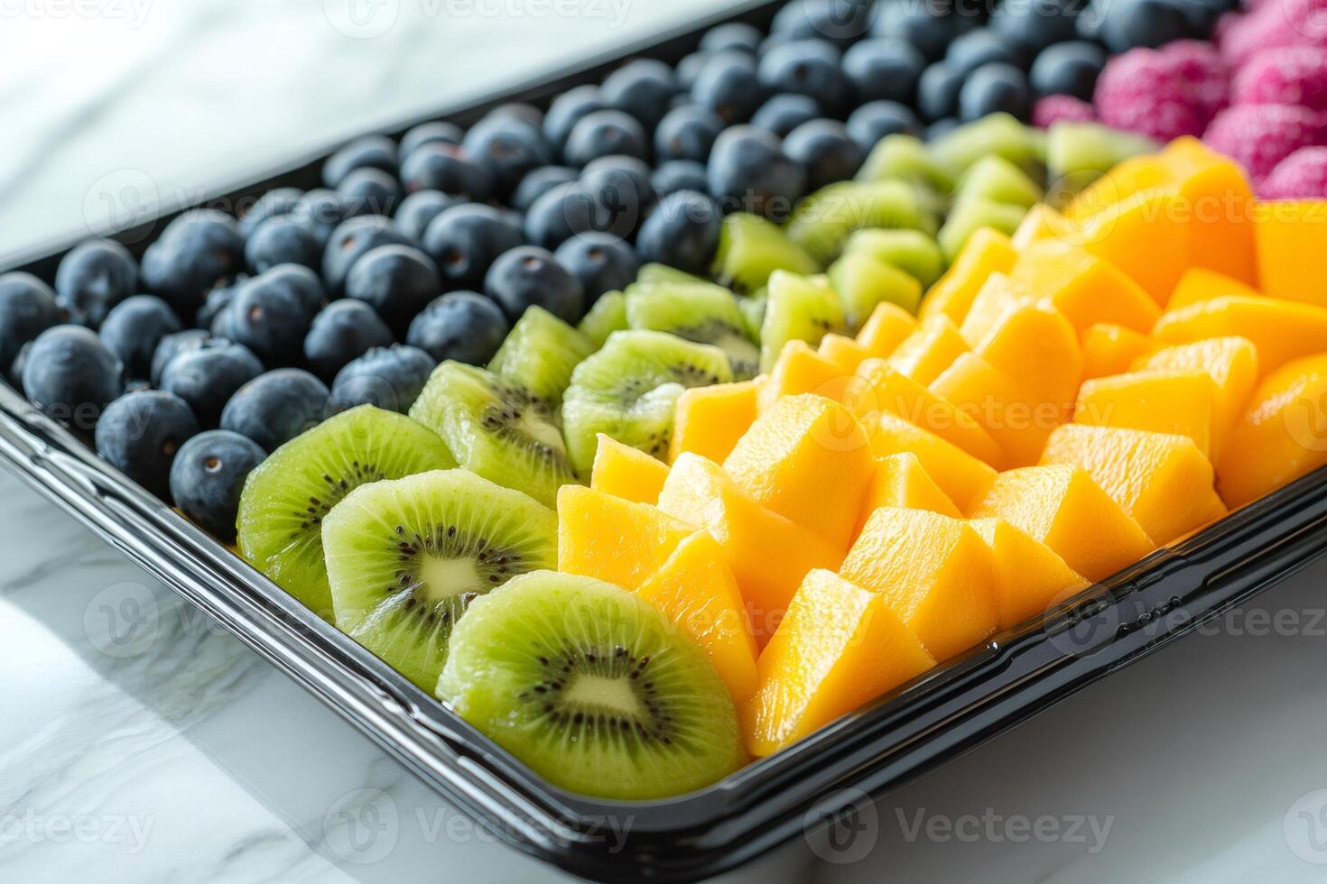 Fresh cut fruit platter with mango, kiwi, blueberries, raspberries arranged in rows on a black catering tray photo