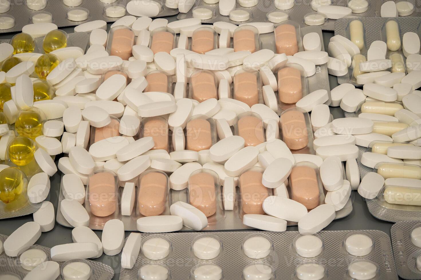 A collection of assorted pills and capsules is spread over a flat surface photo