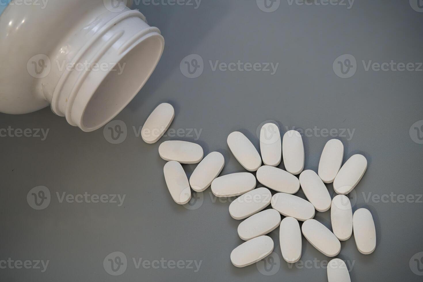 Bottled white tablets scattered on a gray surface after spilling photo