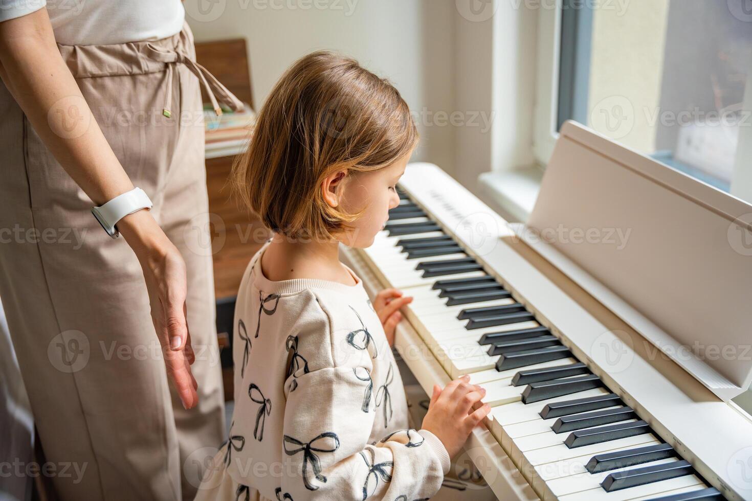Home lesson with teacher on music for girl on white piano synthesizer. Concept of early development. learning music enhances motor skills, hearing, intelligence, fostering creativity from childhood. photo