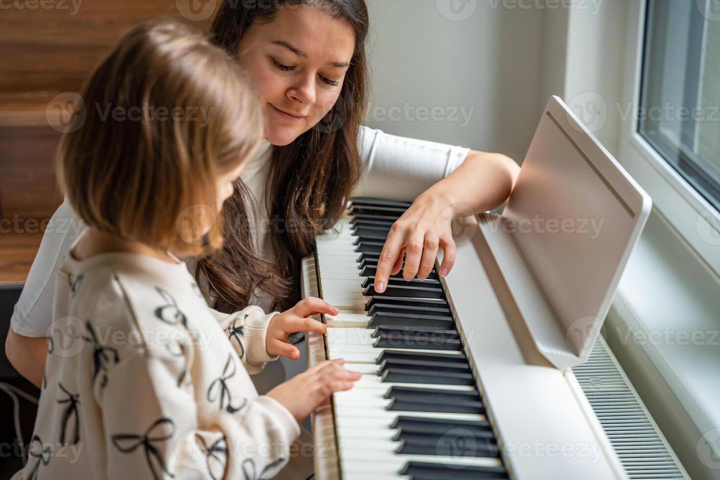 Home lesson with teacher on music for girl on white piano synthesizer. Concept of early development. learning music enhances motor skills, hearing, intelligence, fostering creativity from childhood. photo