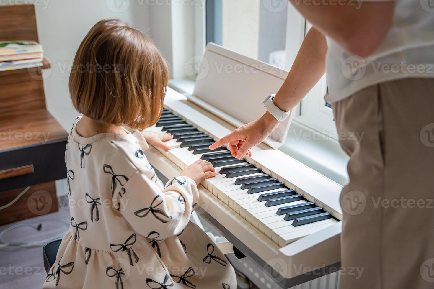 Home lesson with teacher on music for girl on white piano synthesizer. Concept of early development. learning music enhances motor skills, hearing, intelligence, fostering creativity from childhood. photo
