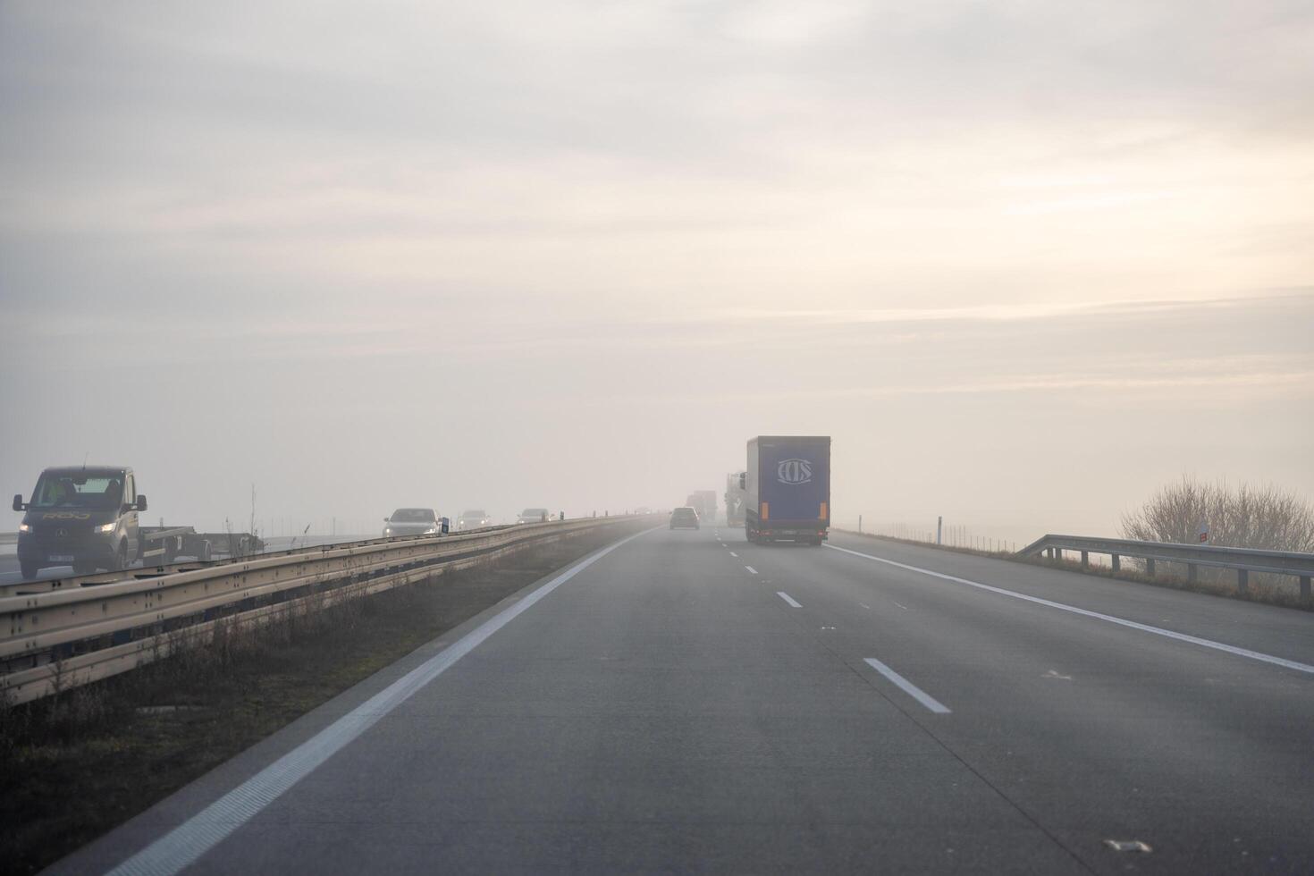 Germany, Europe - 20.12.2024. Back tail view of many cars driving fast on wet highway road in fog in Europe. High quality photo