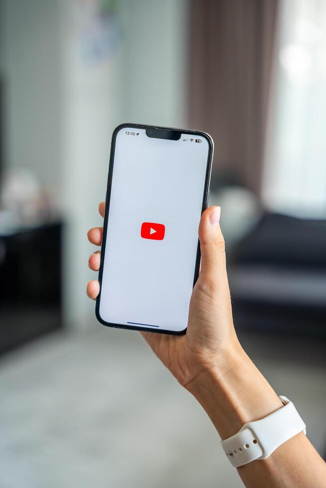 Prague, Czech republic - May 2, 2024. Woman holding iPhone with logo of application YouTube on the screen, using mobile application for business home. High quality photo