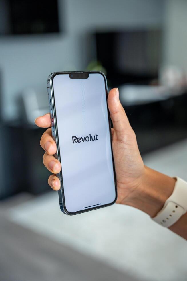 Prague, Czech republic - May 2, 2024. Woman holding iPhone with logo of application Revolute on the screen, using mobile application for business home. High quality photo