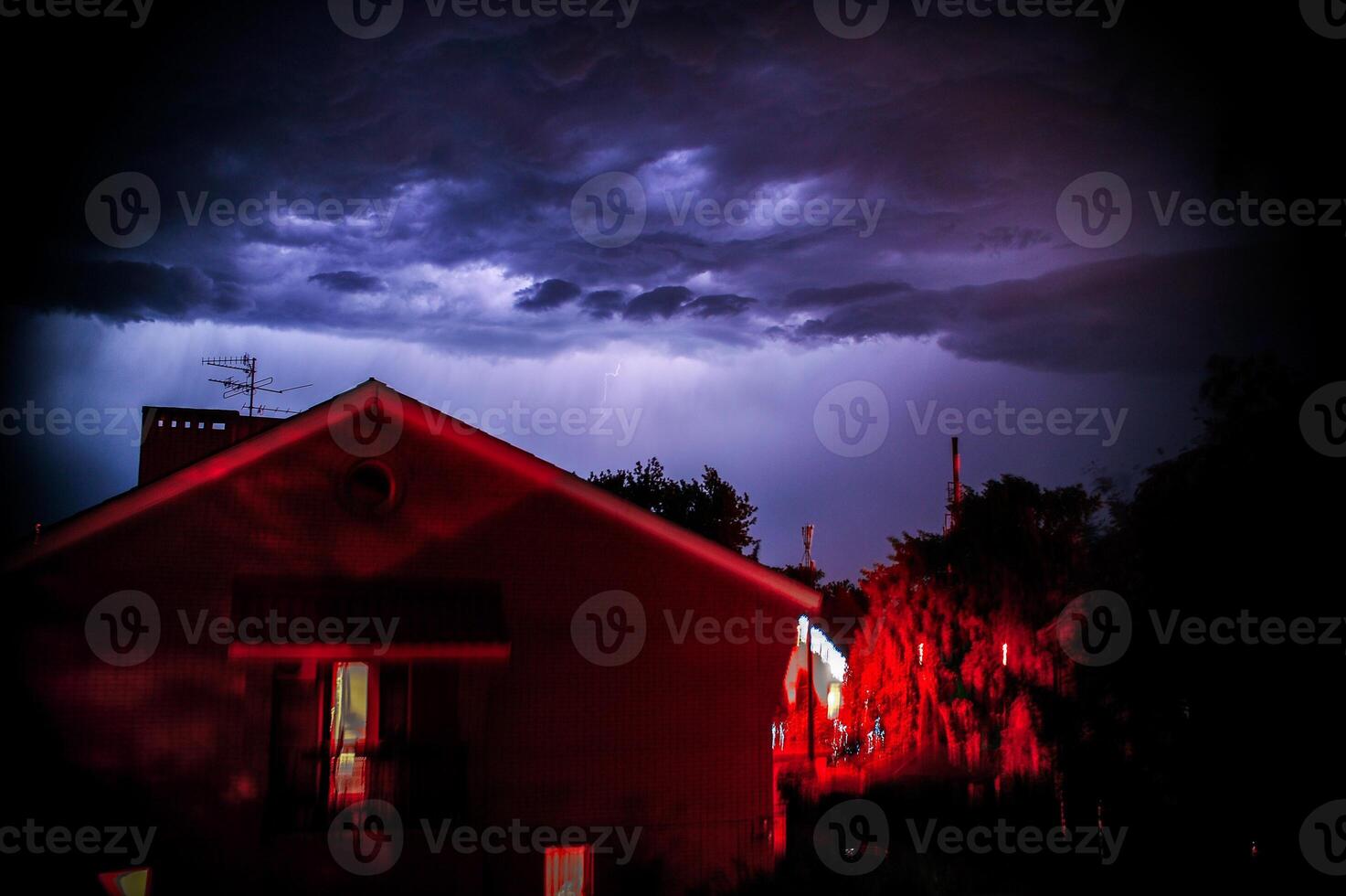 A red house is lit against a stormy sky, creating striking contrast photo
