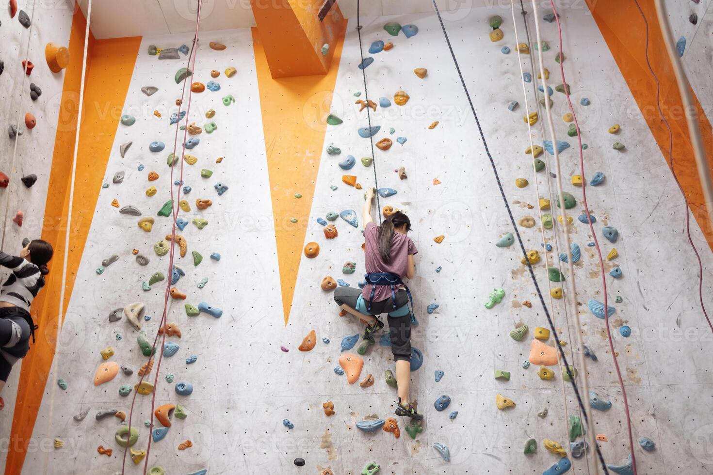 Two multiracial women doing rock climbing in the gym together photo
