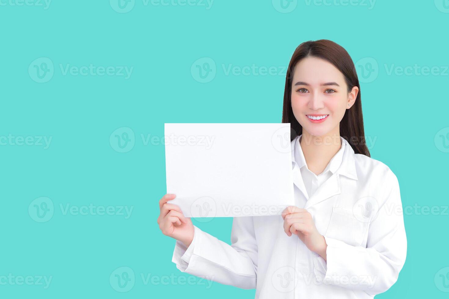 Young professional asian woman doctor who wears medical coat holds and shows white paper to present something in healthcare concept while isolated green background. photo