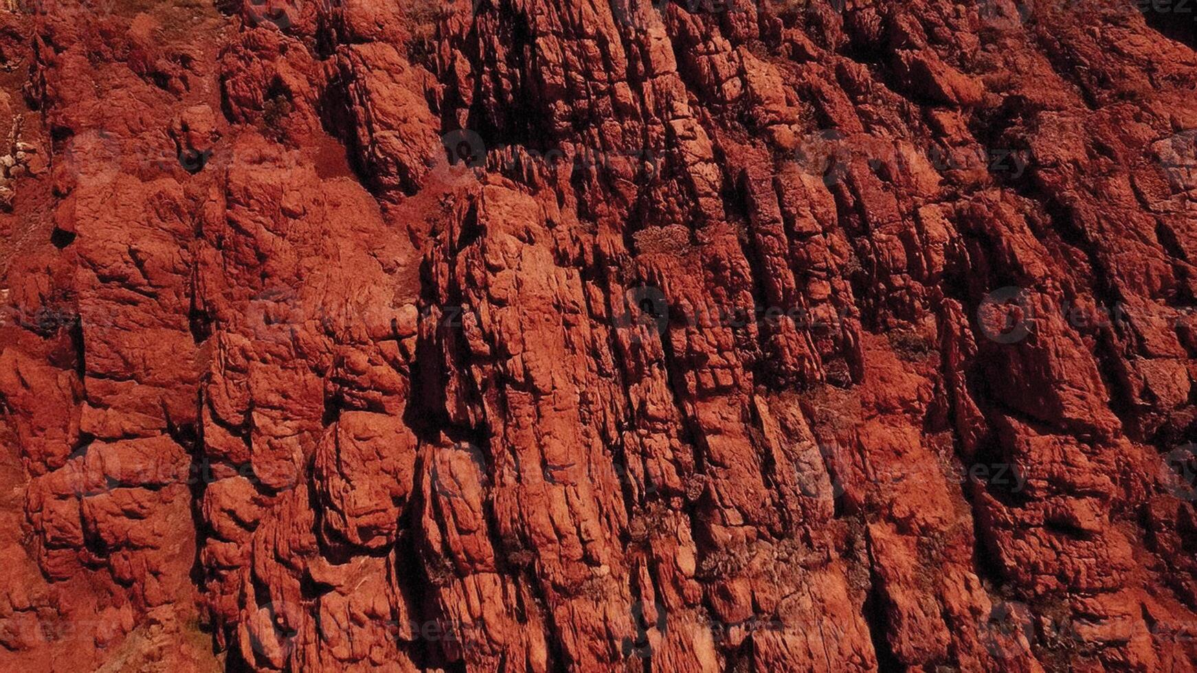 Vivid red rock face with layered formations and intricate fissures, reflecting natural erosion and rugged surfaces ideal for architecture, abstract design, and geological backgrounds. photo