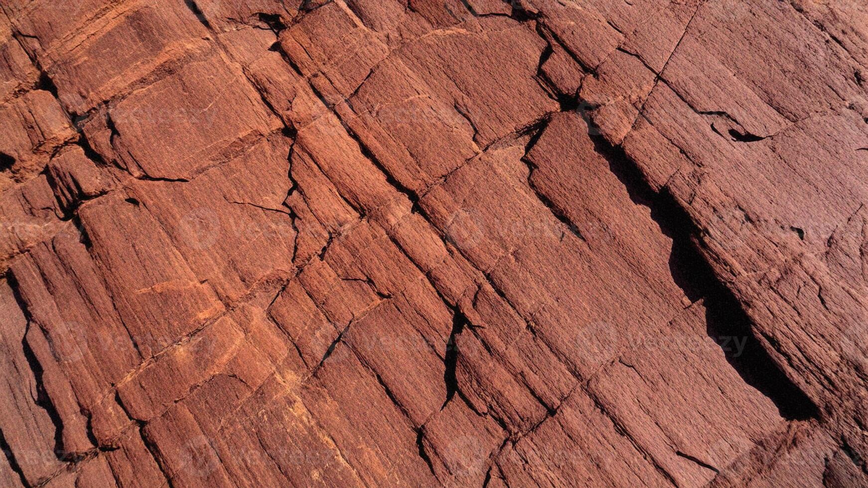 Cracked red rock face with pronounced crevices and rough textures, representing geological beauty suitable for architectural design, backgrounds, and organic pattern projects. photo