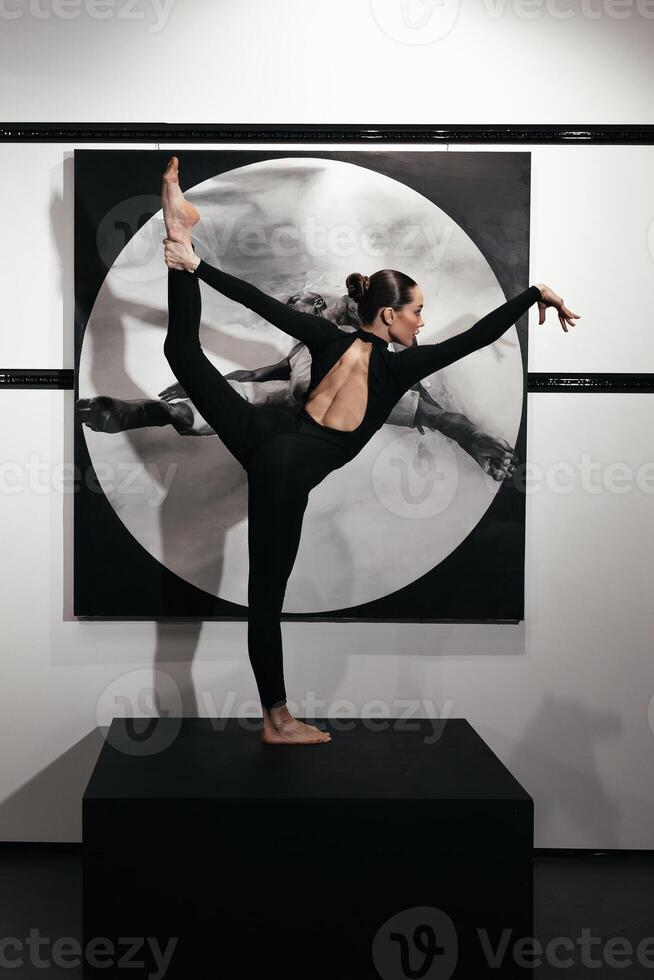 Full length beautiful gymnast in black suit is posing on black podium in backlight. The grace, artist, movement, action and motion concept. Looks weightless, flexible. How art become action. Vertical photo