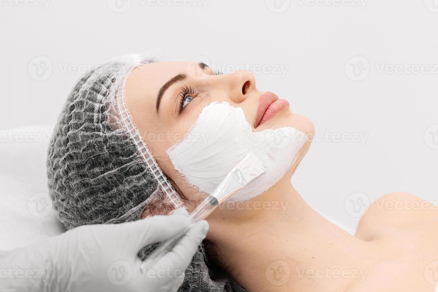 A serene woman receiving a moisturizing facial mask applied by a beautician in a spa setting. Beautician making beauty facial skincare procedure to patient. Beauty industry concept photo
