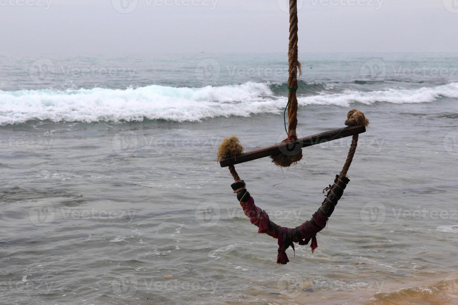 rope swing hanging on tropical beach with waves crashing on shore on cloudy day. Background, summer beach activities photo