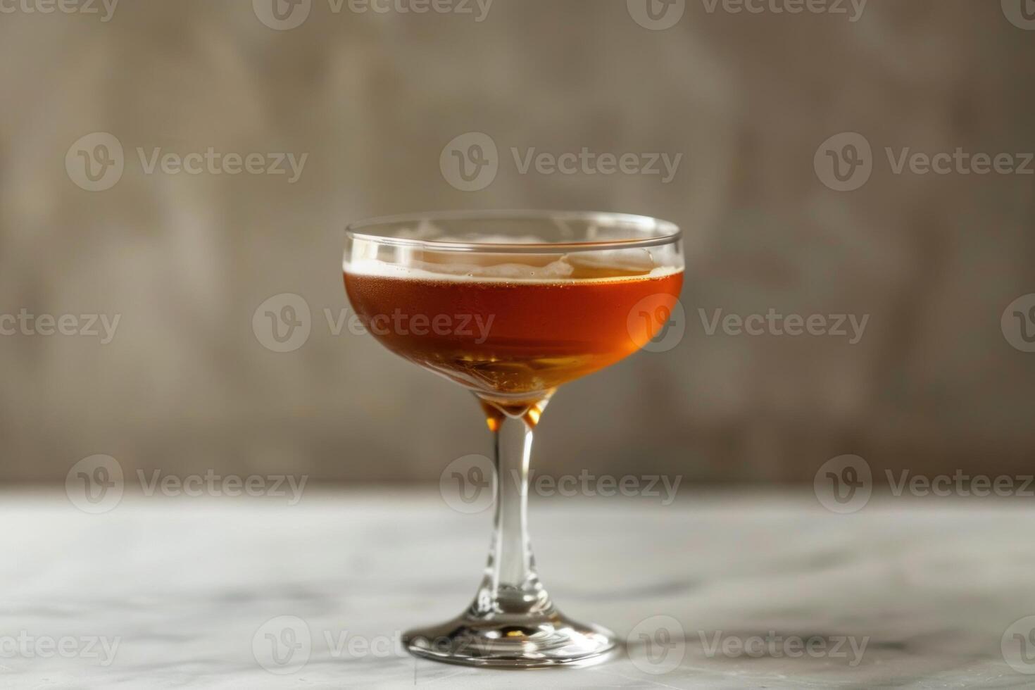 Coupe glass containing brown cocktail on marble surface with blurred background photo