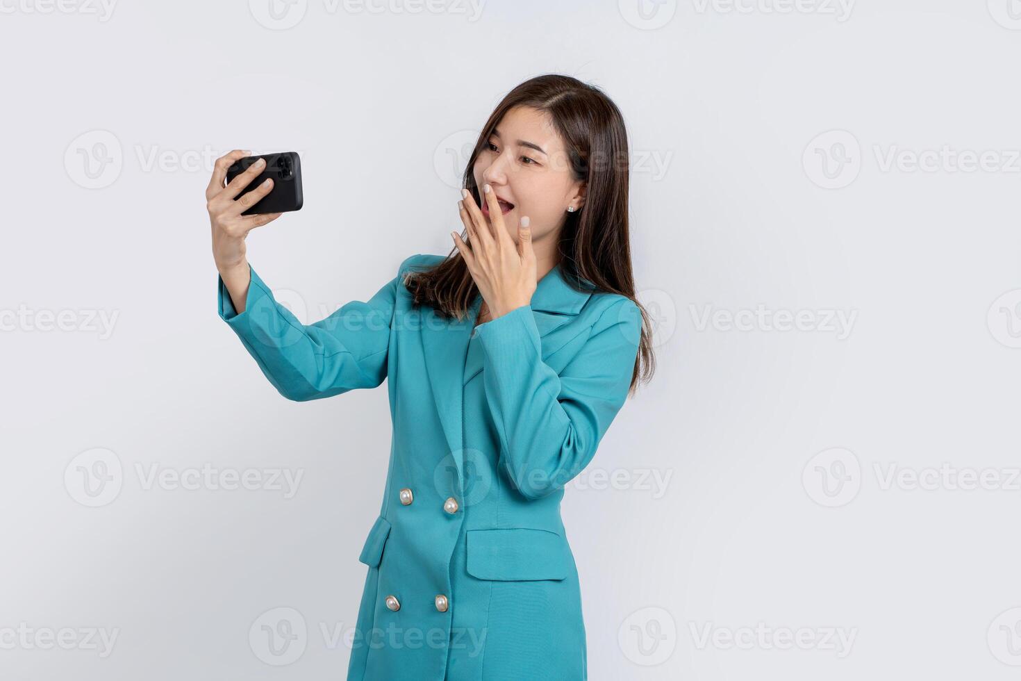 Surprised Asian woman in bright green suit holding smartphone isolated on white background. She looked at the phone screen. photo