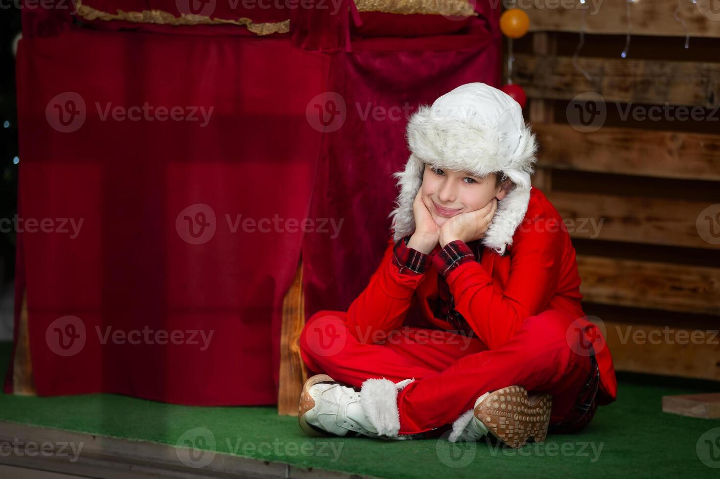 A funny boy in a Christmas red suit and a fur hat looks at the camera. A child at a carnival. photo