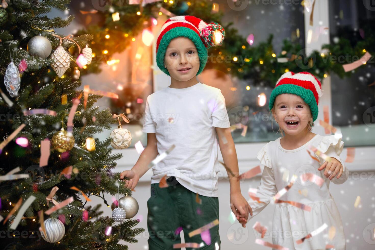 Children enjoy the Christmas holiday and look at the magical golden confetti in the Santa Claus hat. photo