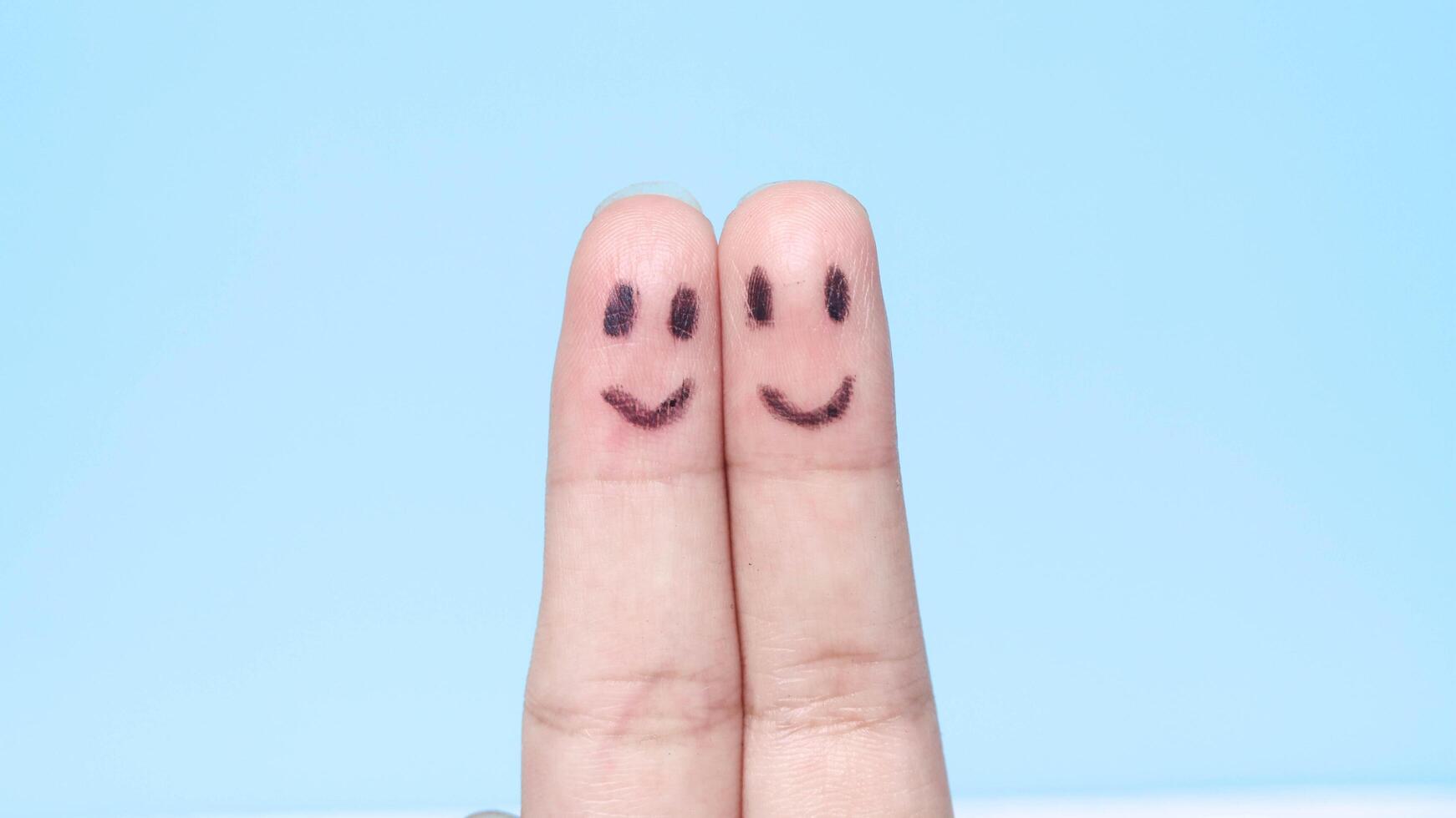 Two fingers with a happy face drawn like family or friends, a finger with a smiling emoji, a finger with a face photo