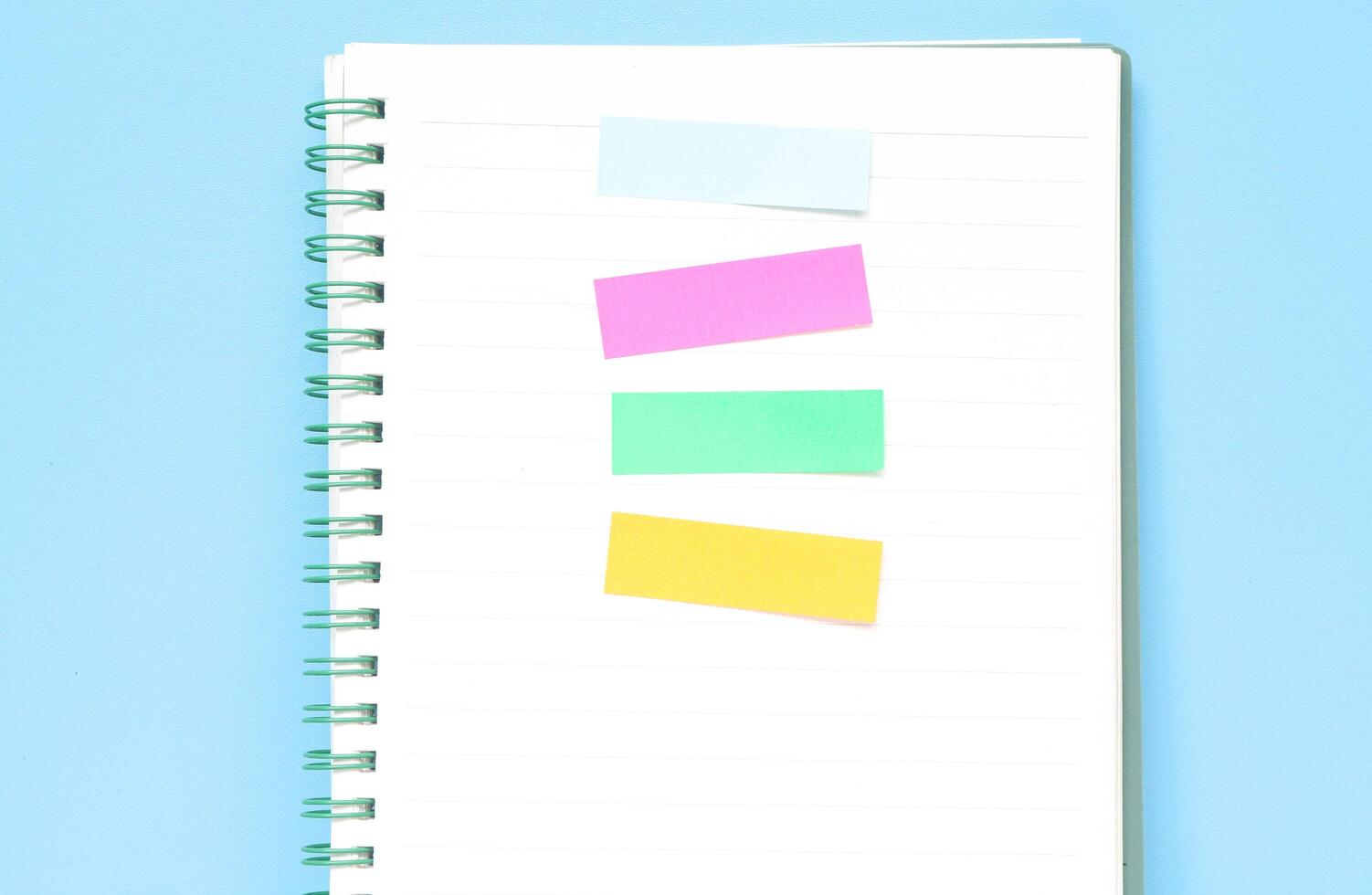 Four colored markers in a notebook on a wooden table. Colorful post paper notes or bookmarks on gray background. Journaling and office desk concept photo