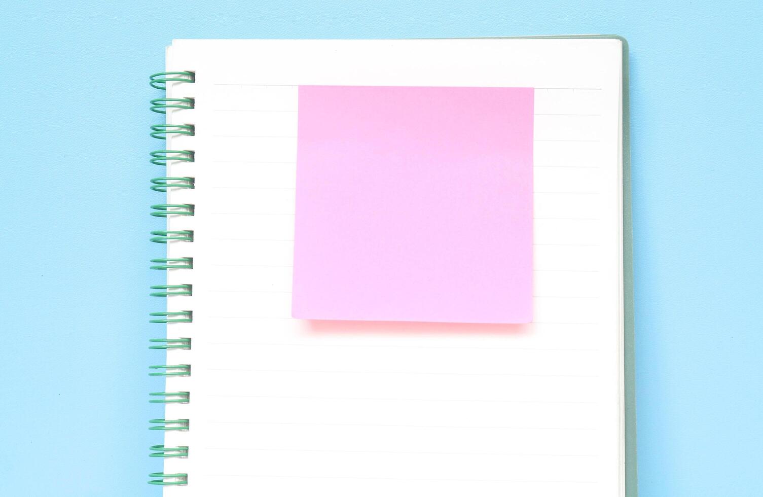 Pink sticky note on a notebook isolated with blue background. Journaling and office desk concept with copy space photo