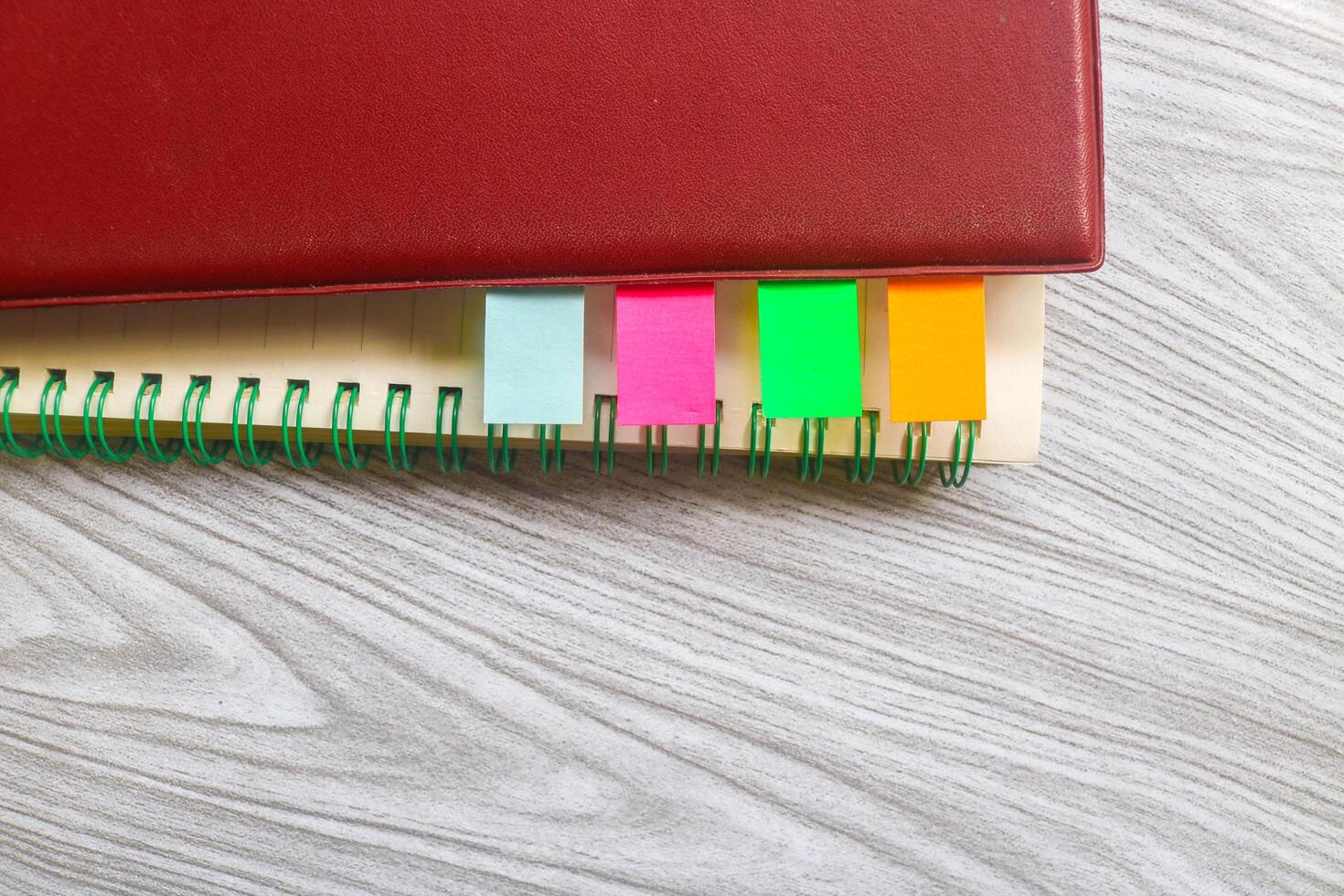 Four colored markers with notebooks on a wooden table. Colorful sticky note bookmarks were attached to two notebooks. Journaling and office desk concept photo