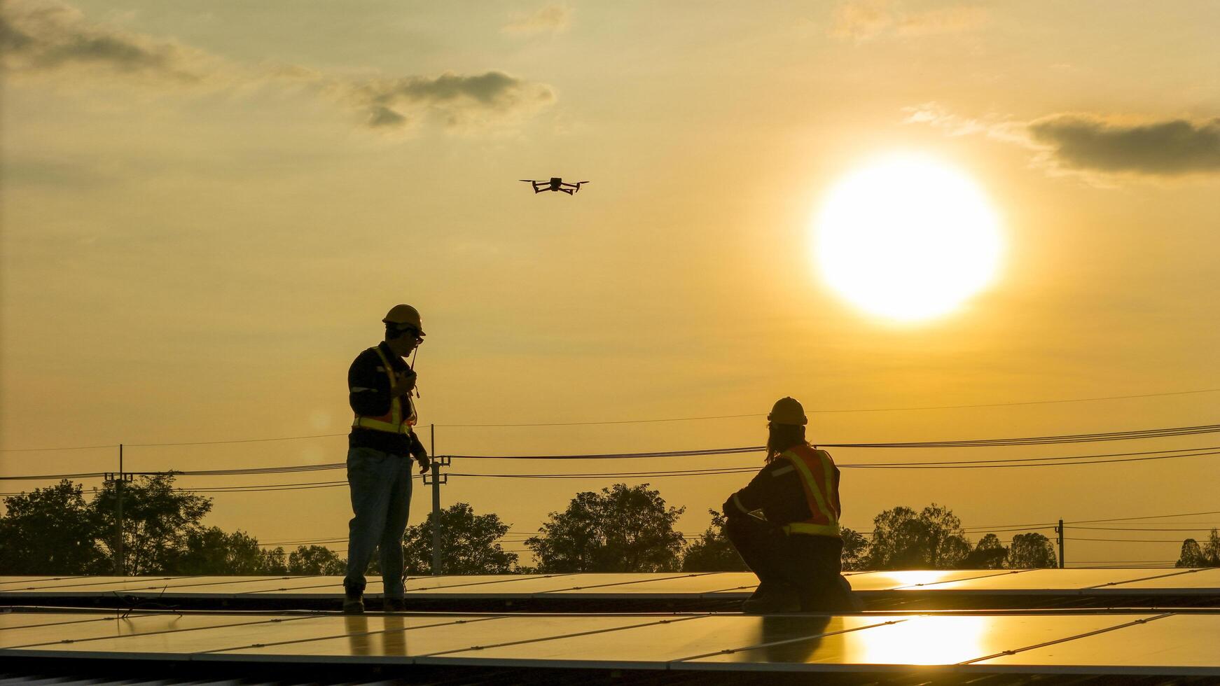 Silhouette of workers ins talling solar panels on a rooftop during sunset with a drone hovering nearby, highlighting renewable energy, innovation, and sustainable practices in solar technology. photo