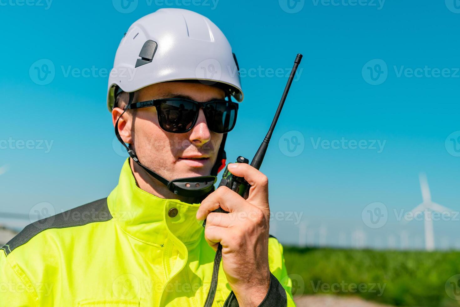 Worker in safety gear using a radio near wind turbines on a sunny day photo