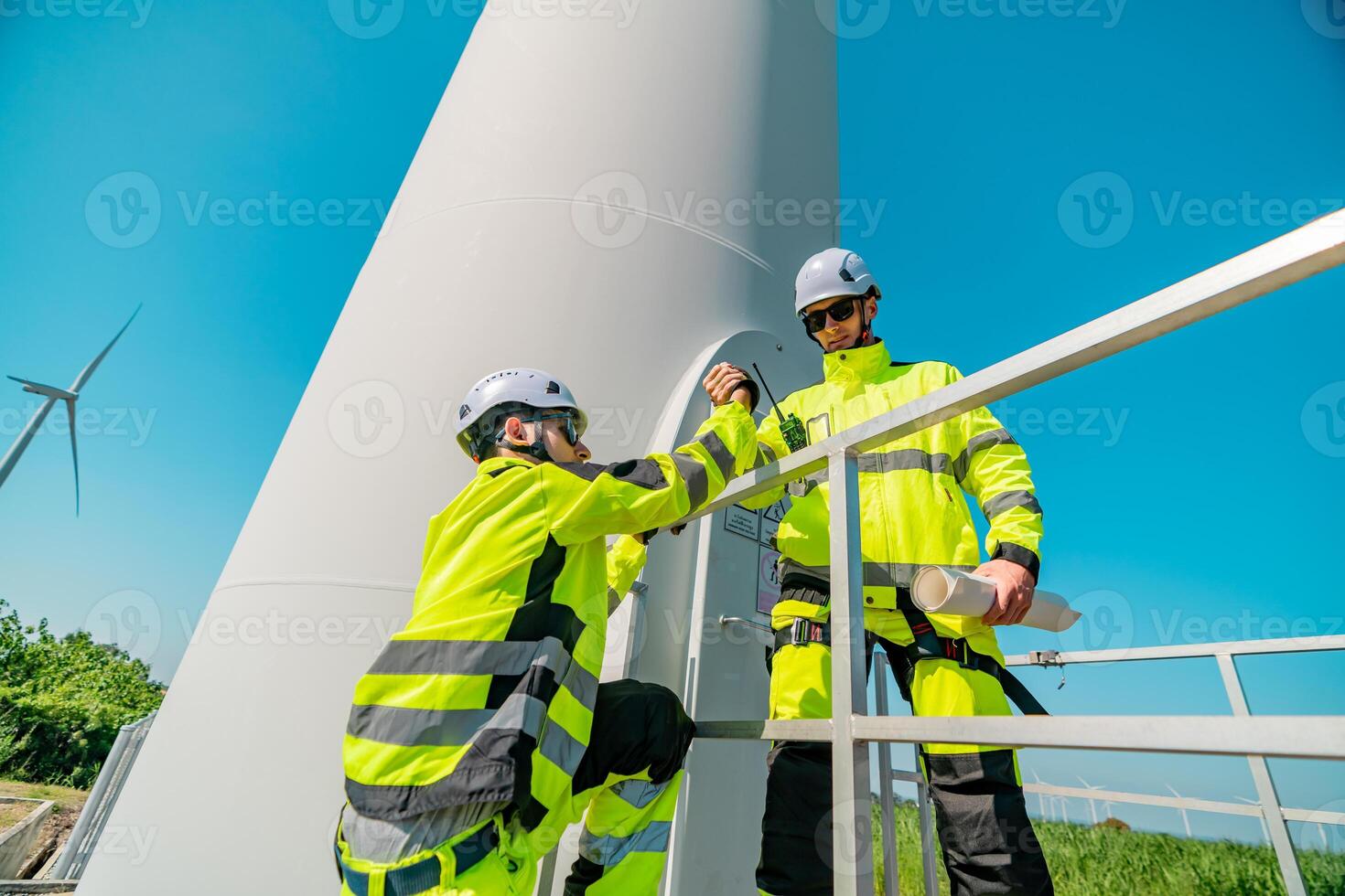 Workers performing maintenance on a wind turbine in bright yellow safety gear under a clear blue sky photo