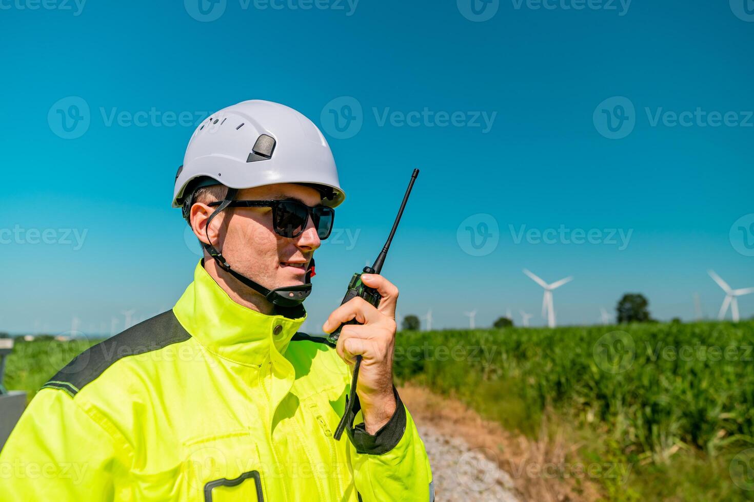 Worker in high visibility jacket communicates with radio near wind turbines on a clear sunny day photo