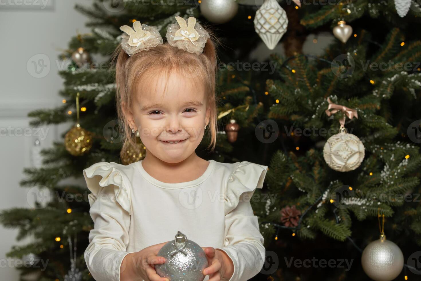 Funny little girl with a Christmas ball on the background of a Christmas tree. photo