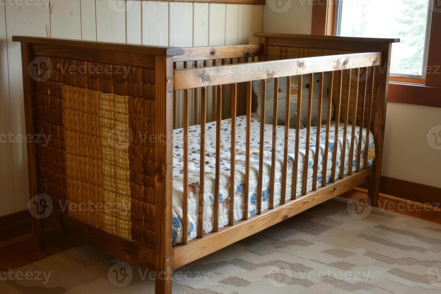 Empty wooden baby crib with quilt standing on rug in nursery photo