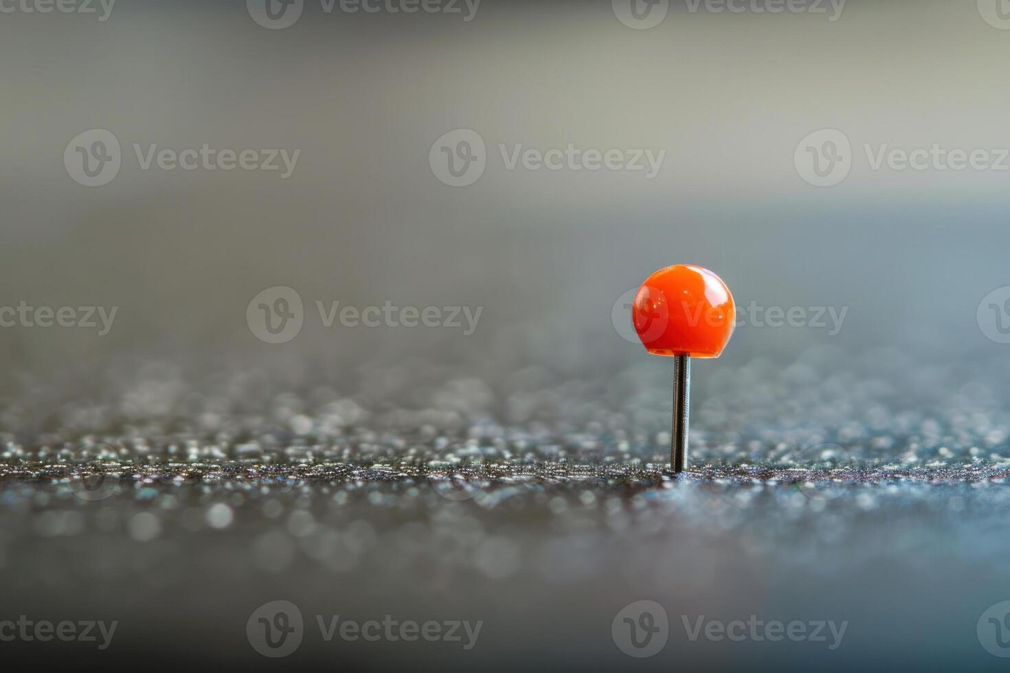 Orange push pin standing on a black surface photo