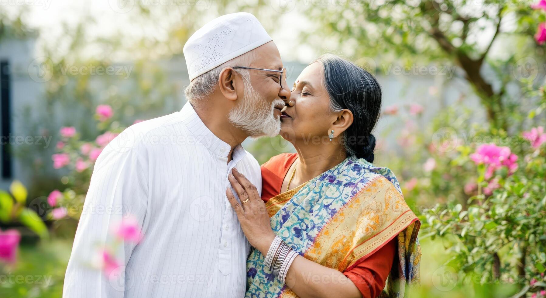 Elderly south asian couple sharing a joyful romantic moment in a garden surrounded by vibrant pink flowers photo