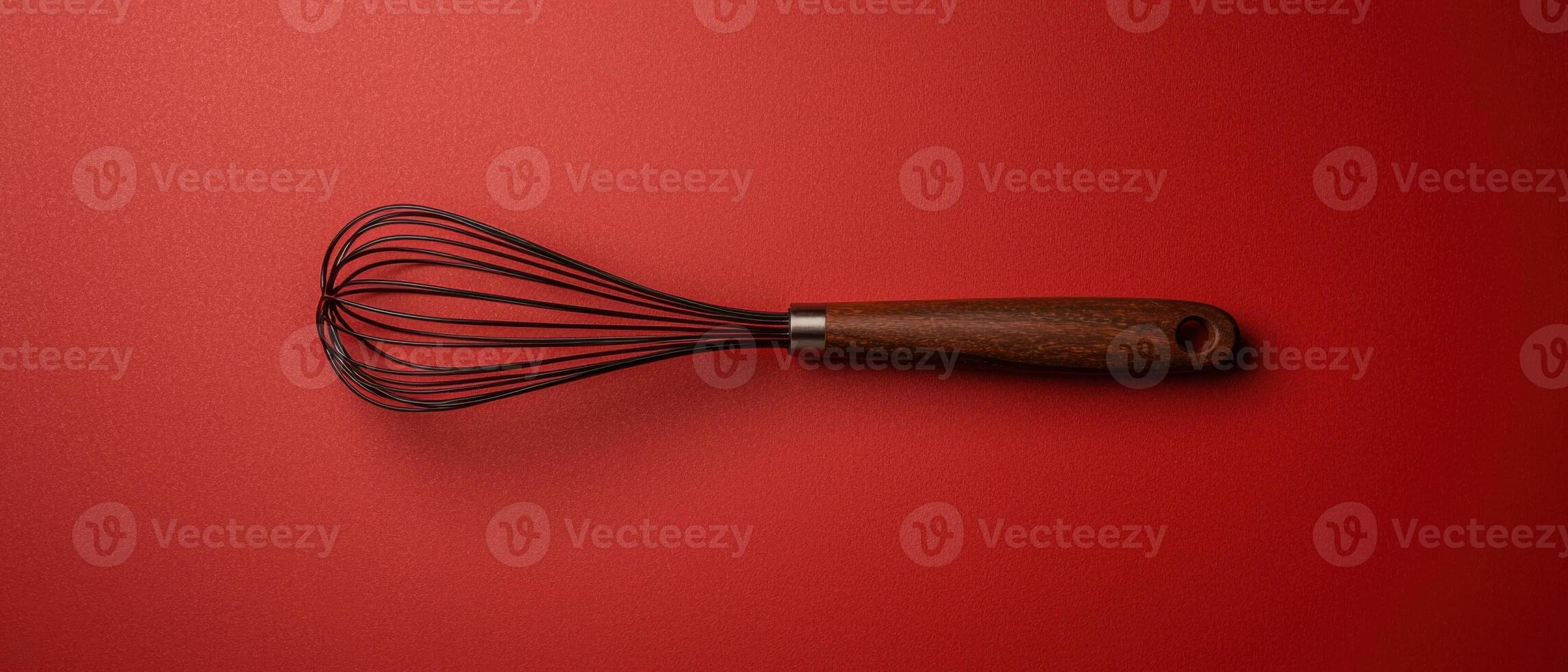 Wooden handled whisk on red background photo