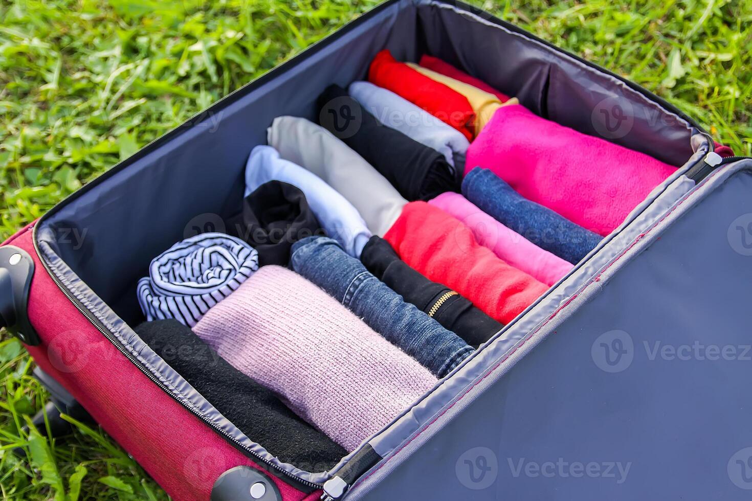Open suitcase on the grass with different clothes folded vertically. Vertical storage for easy travel packing. photo