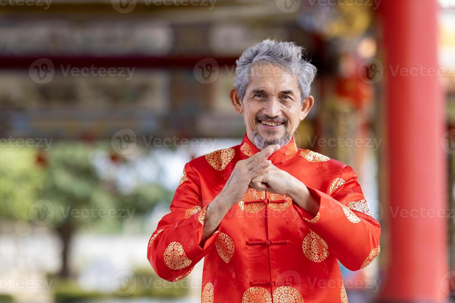 Asian senior elder man in red cheongsam qipao cloth is doing respect gesture inside the Chinese Buddhist temple during lunar new year for best wish blessing usage photo