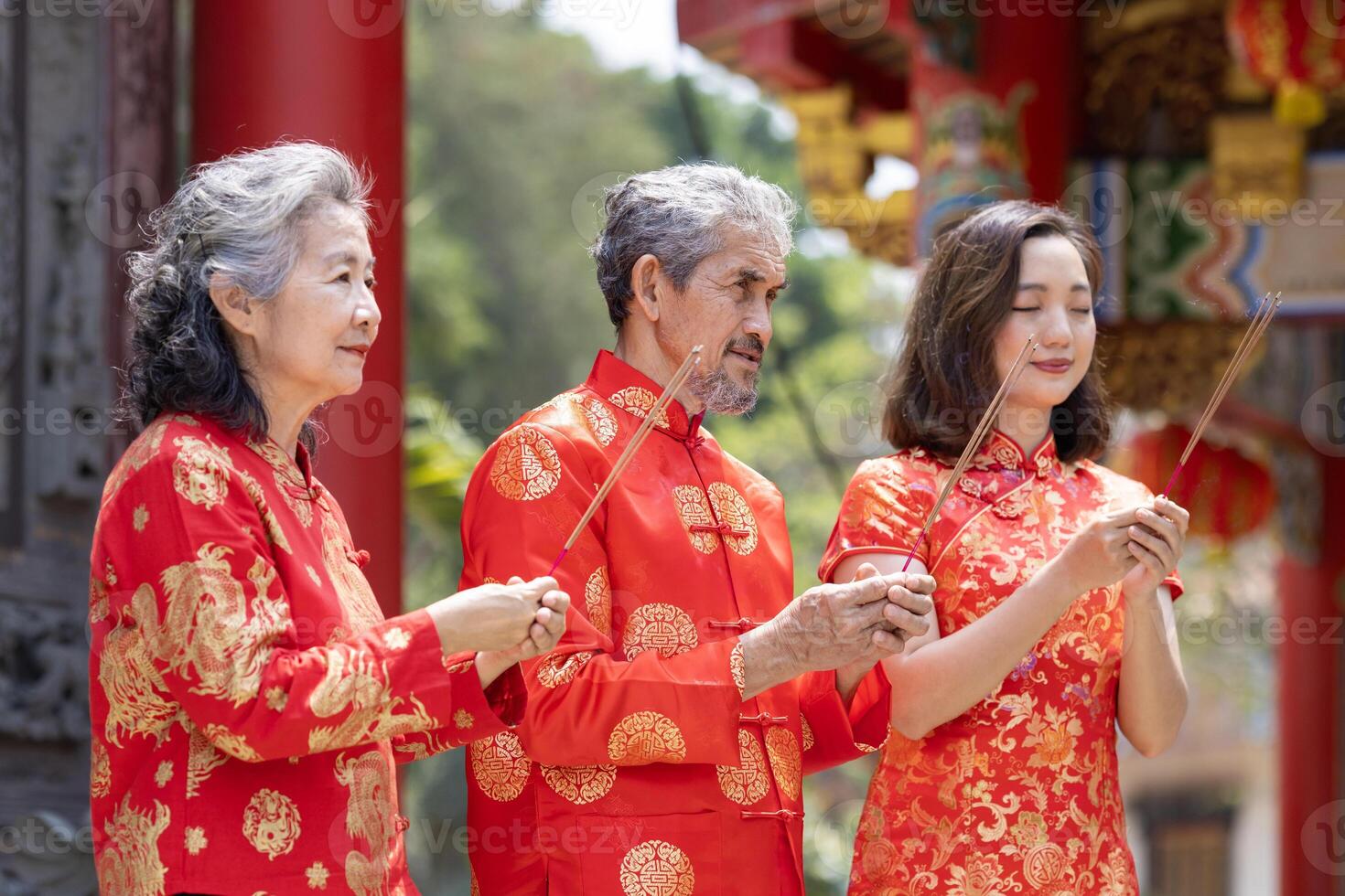 Asian family with senior parents in red cheongsam qipao dress is offering incense to the ancestral god inside Chinese Buddhist temple during lunar new year for best wish blessing and good luck usage photo