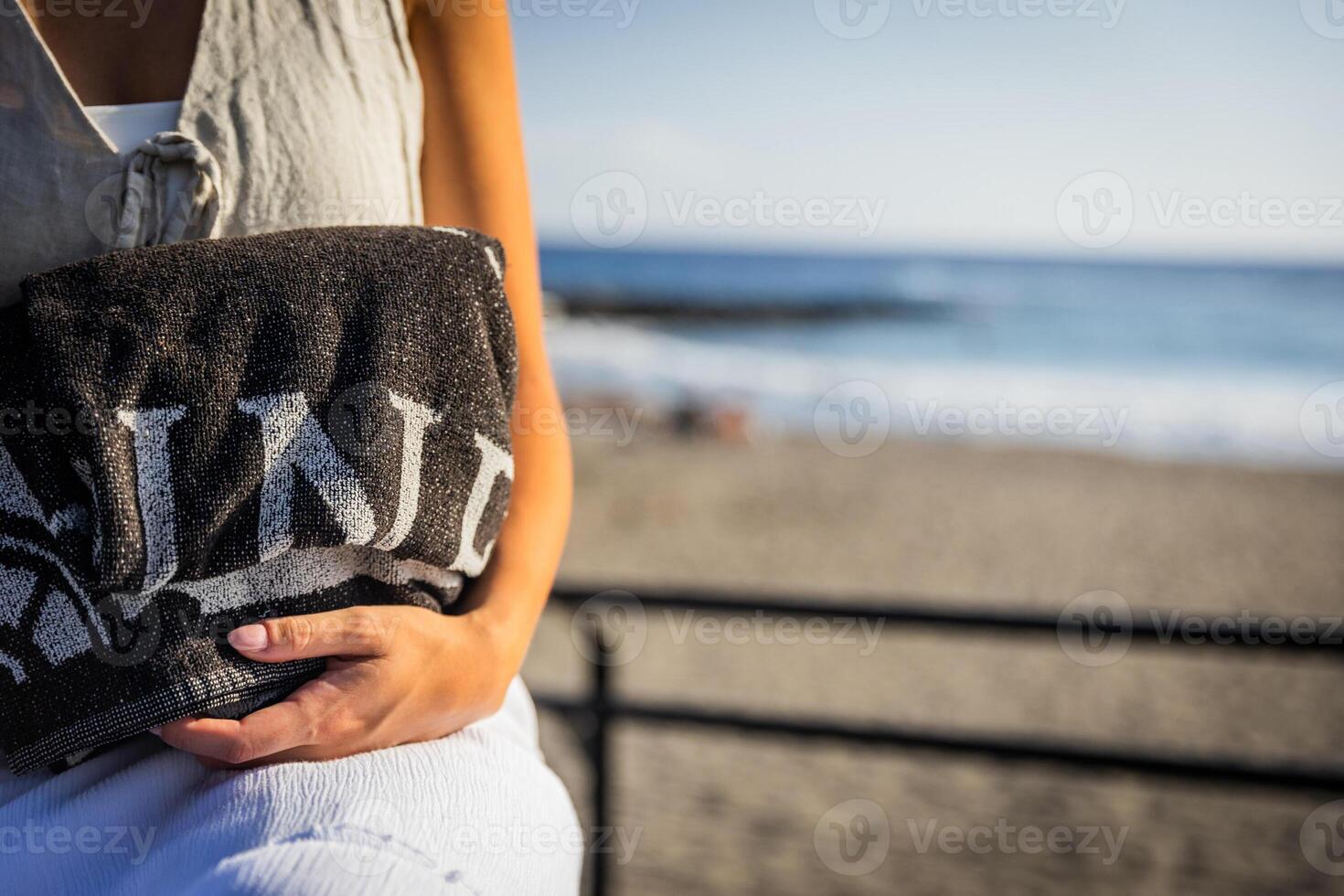 A woman is holding a black and white towel at the beach, beach vibes photo