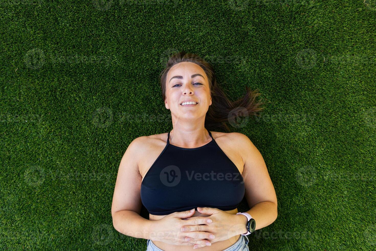A woman is laying on the grass with her arms crossed and a smile on her face photo