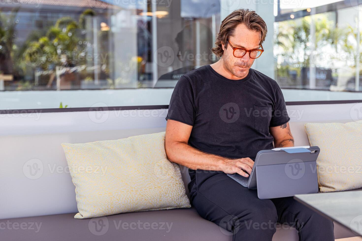 A concentrated man is sitting on a couch working on his tablet, photo with copy space