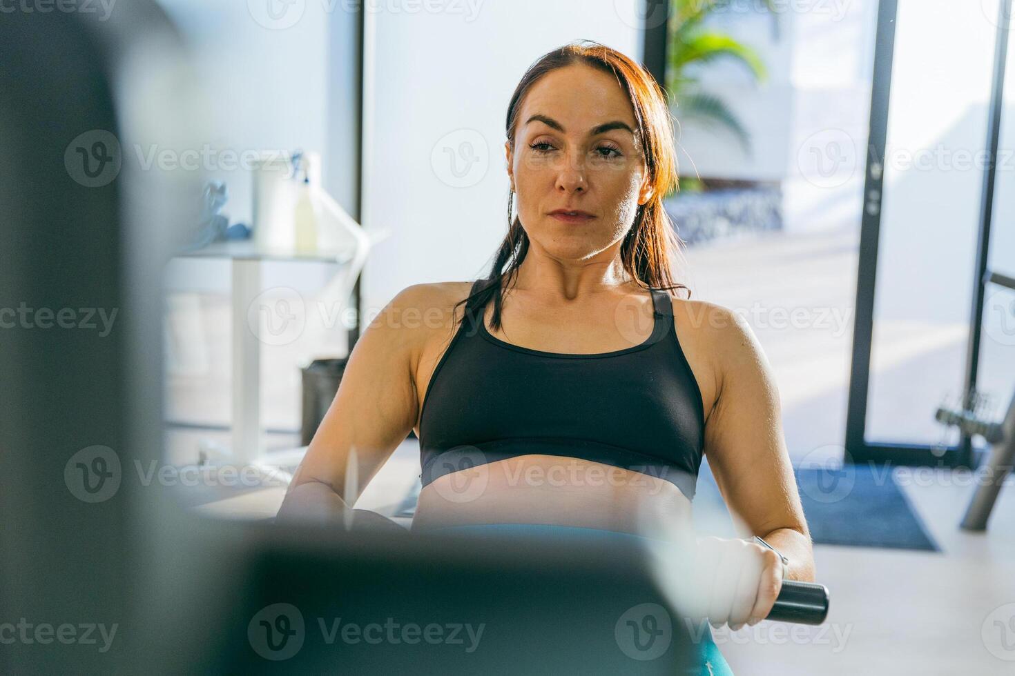 A woman is exercising on a rowing machine in the gym, portrait of her face focused photo