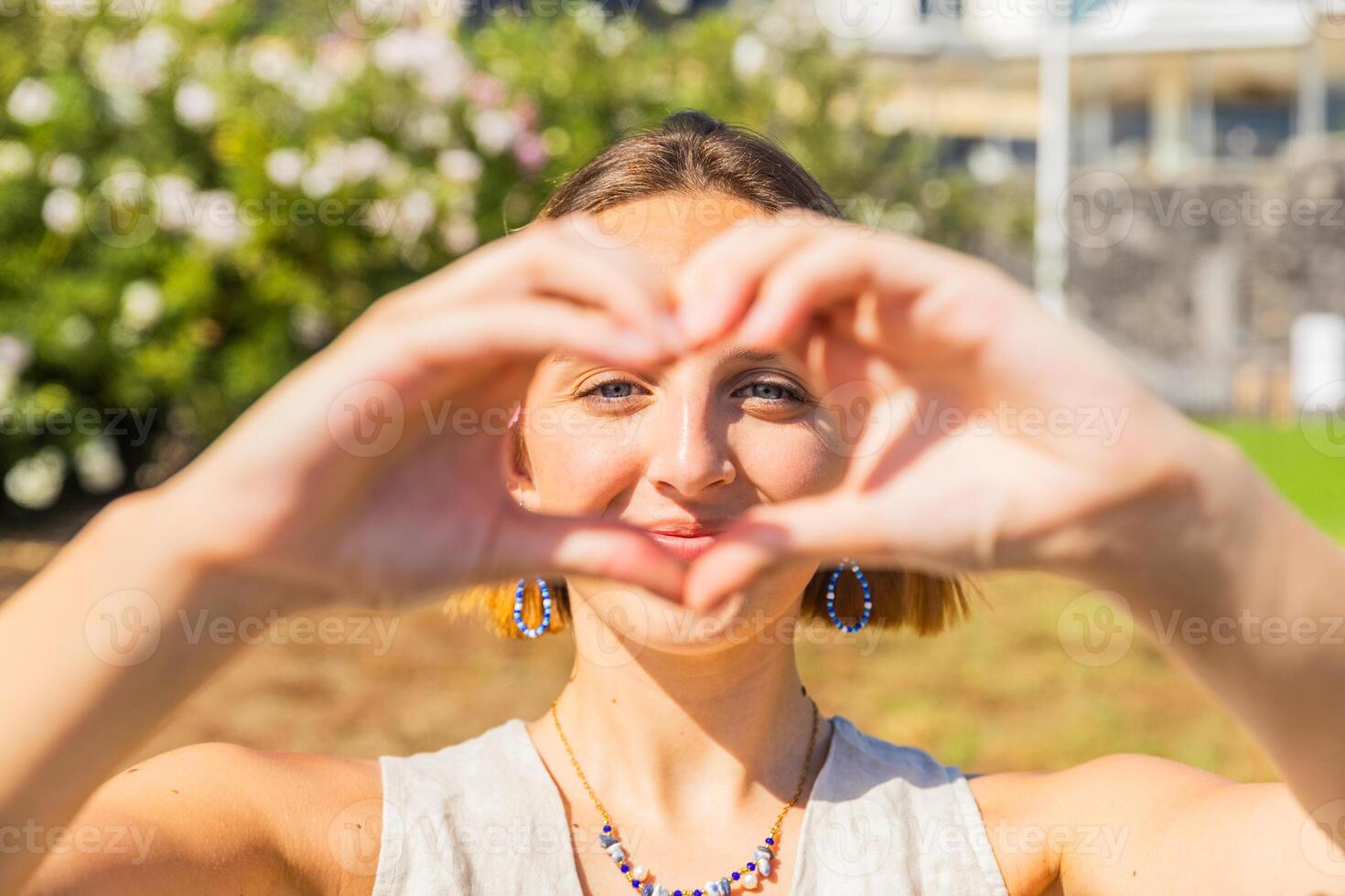 A woman is smiling and holding her hands together in a heart shape, happy girl outdoors in summer photo