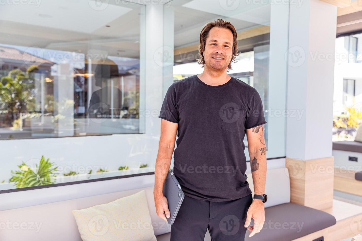 A businessman casually dressed is holding a tablet and smiling photo