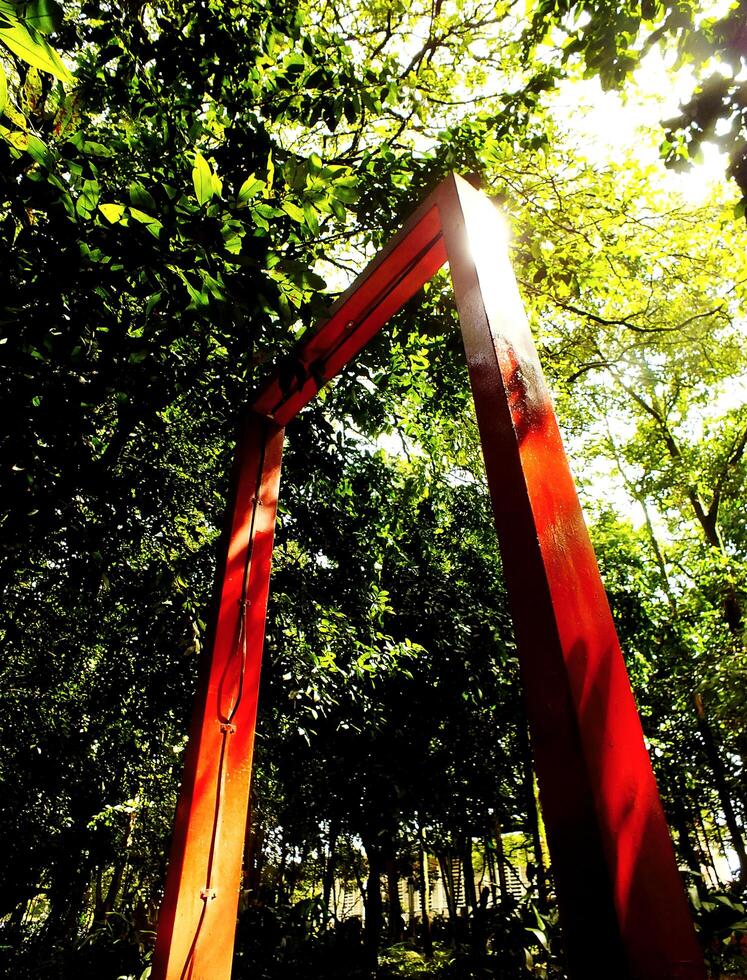 low angle view. Red archway in a forest with sunlight shining through it. The archway is surrounded by trees and bushes, creating a serene and peaceful atmosphere photo