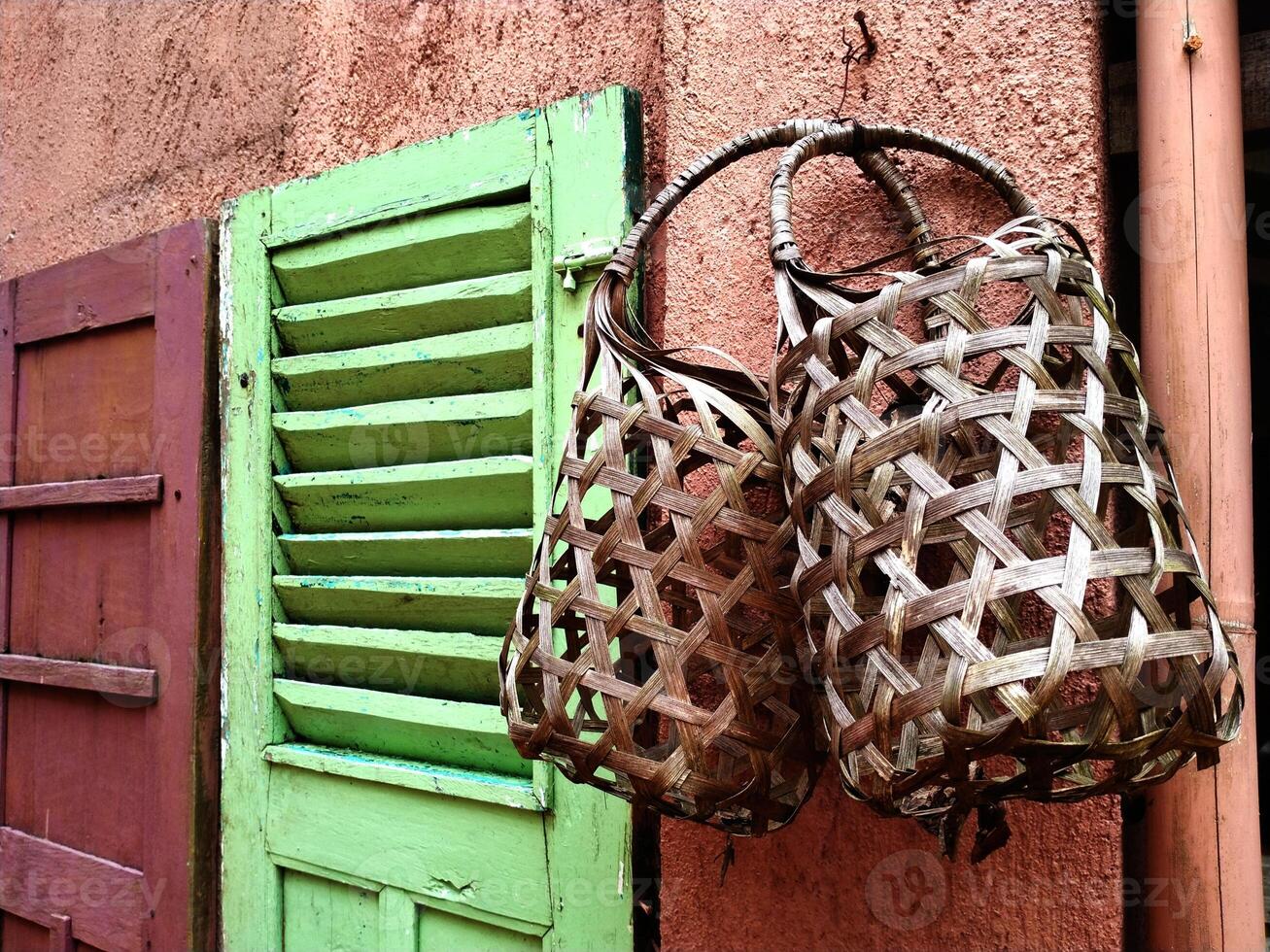Two baskets made from woven bamboo, hanging on the pink wall. There is a green wooden window photo