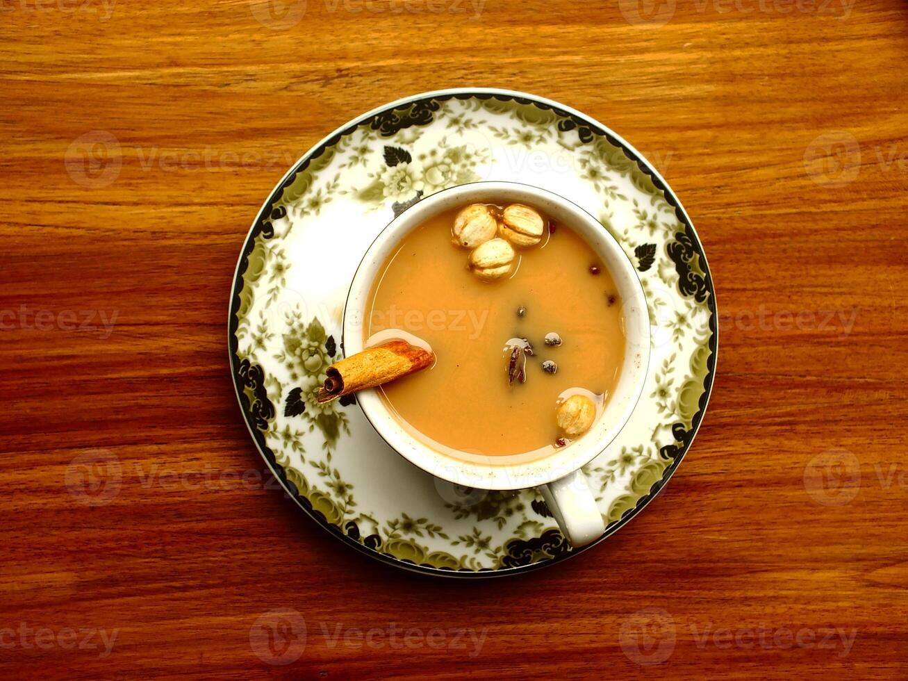 Flat lay. Top angle view. Cup of tea with cinnamon on top of a white cup on a wooden table. The tea is hot and the cinnamon adds a warm and comforting flavor photo