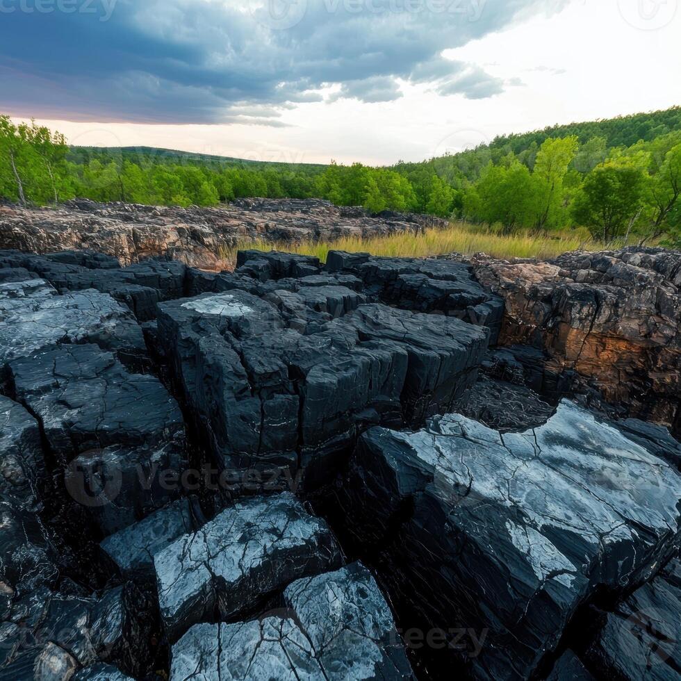 Dark basalt columns and green forest under a dramatic sky photo