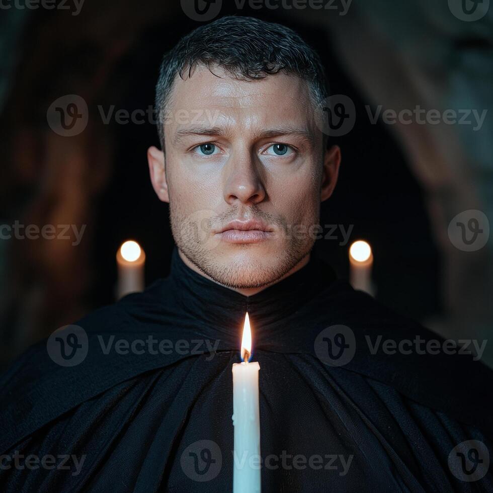 Man in black robe holds a candle in a dark room photo
