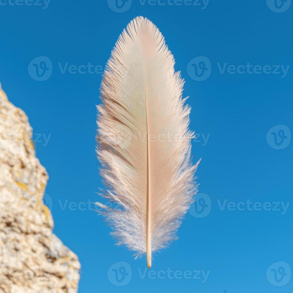 Single feather floating against a blue sky photo