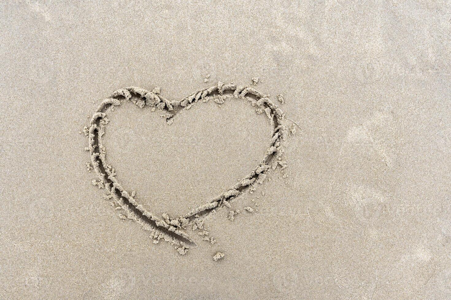 Symbol of heart written by hand on sand of beach with copy space photo